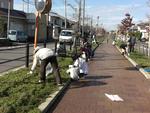 茶色の歩道の脇の花壇を二人の人が清掃している写真