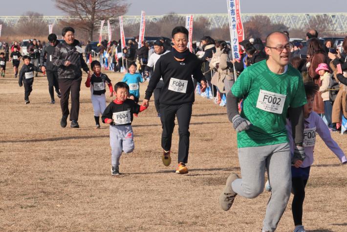 ゼッケンをつけた親子が手をつないで走っています