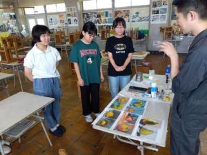 中学生3人が静物の描き方についての説明を聞いています。
