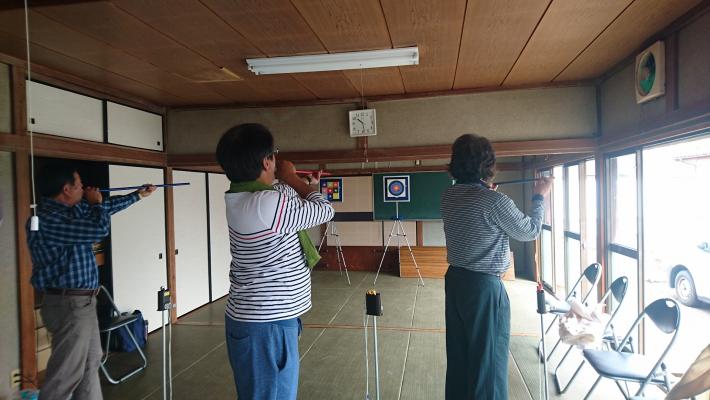 室内でのアーチェリー様のスポーツを楽しむ3人の人の後ろ姿